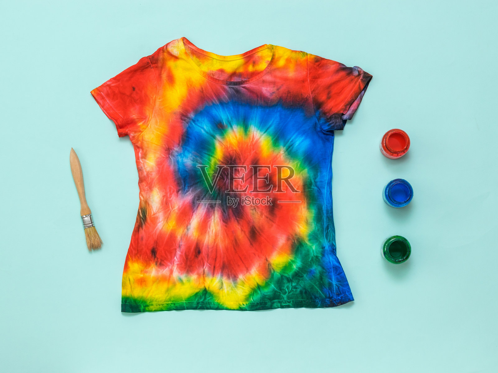 一把刷子，三罐颜料，一件蓝色背景的扎染t恤。平的。照片摄影图片