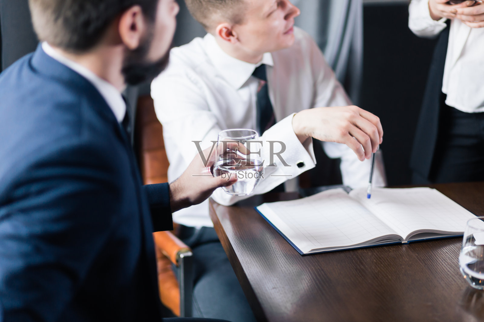 一排人手握着笔做笔记，旁边放着一杯水照片摄影图片