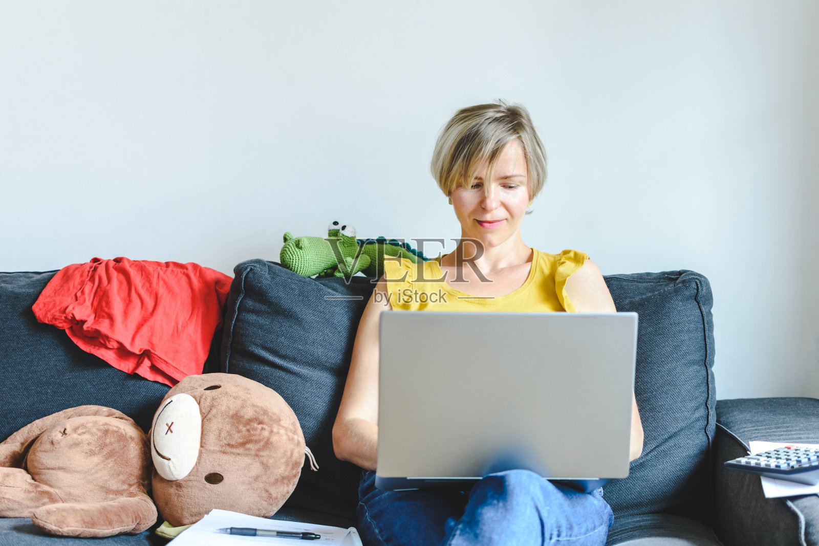 金发母亲坐在沙发上使用笔记本电脑（儿童居家办公）照片摄影图片