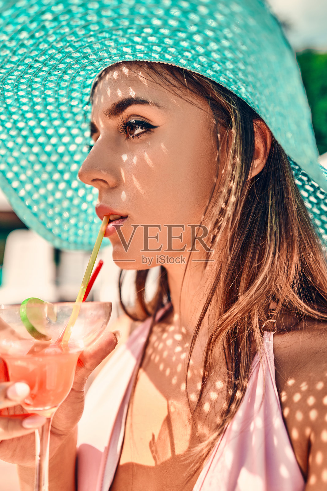 年轻女子戴着帽子，拿着鸡尾酒杯在泳池边照片摄影图片