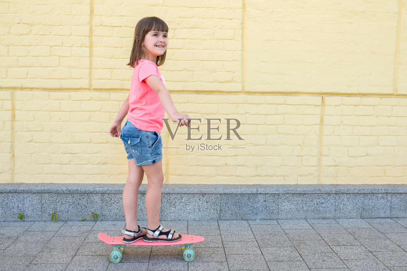 一个可爱的女孩正在玩滑板，背景是一面黄色的墙。运动的生活方式。照片摄影图片