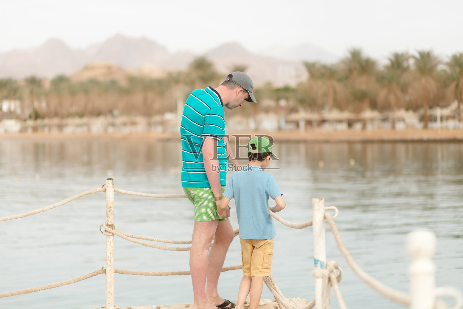 父子站在海滩的栅栏旁，父亲节照片摄影图片