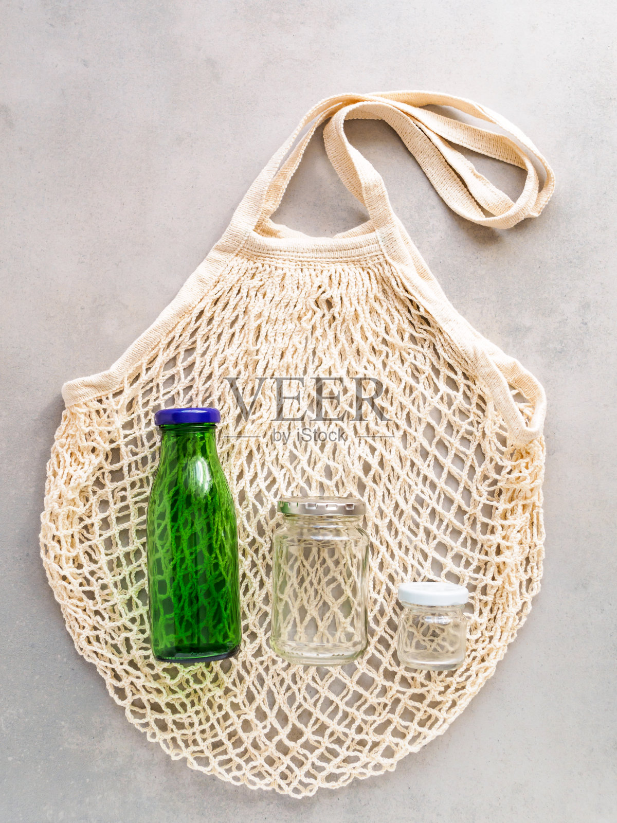 可重复使用的网状购物袋与一个绿色的玻璃瓶和一个梅森瓶在一个灰色的背景，俯视图照片摄影图片