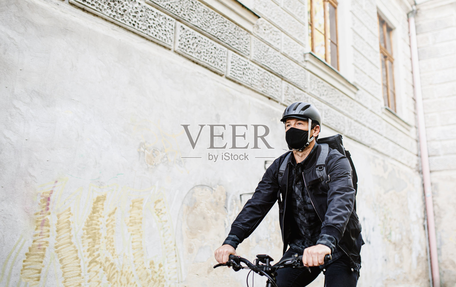 快递员戴着口罩骑着自行车在城里用智能手机。照片摄影图片