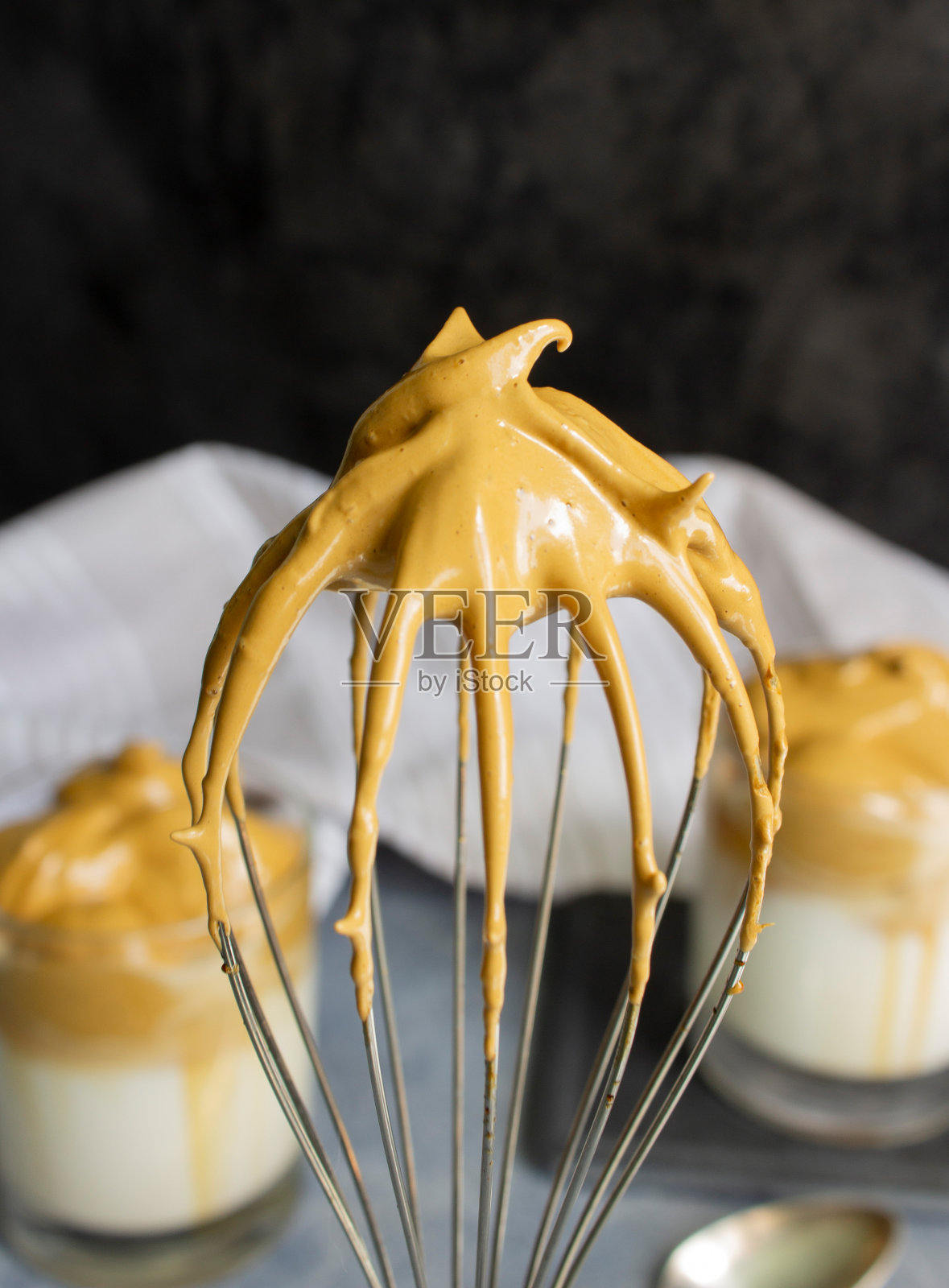 煮完达尔戈纳咖啡后与咖啡泡沫一起搅拌。背景是两杯dalgona /发泡咖啡照片摄影图片