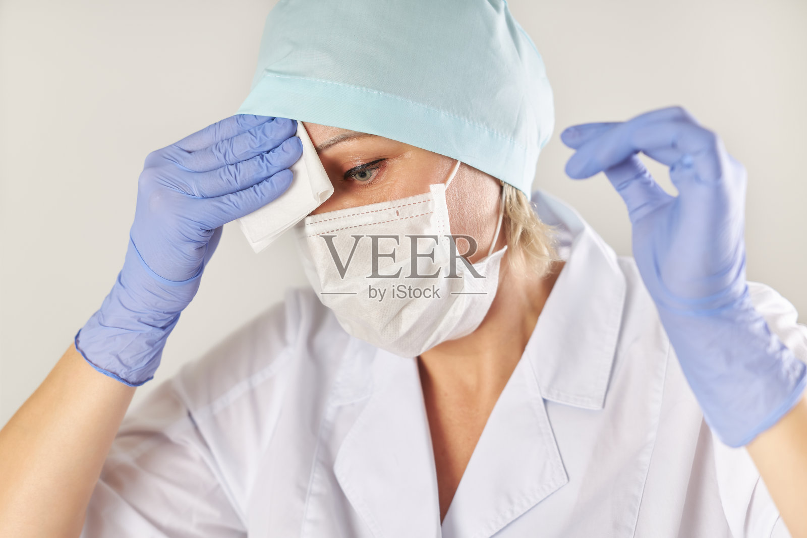女医生戴着医用口罩和手套，用餐巾擦拭额头上的汗水照片摄影图片