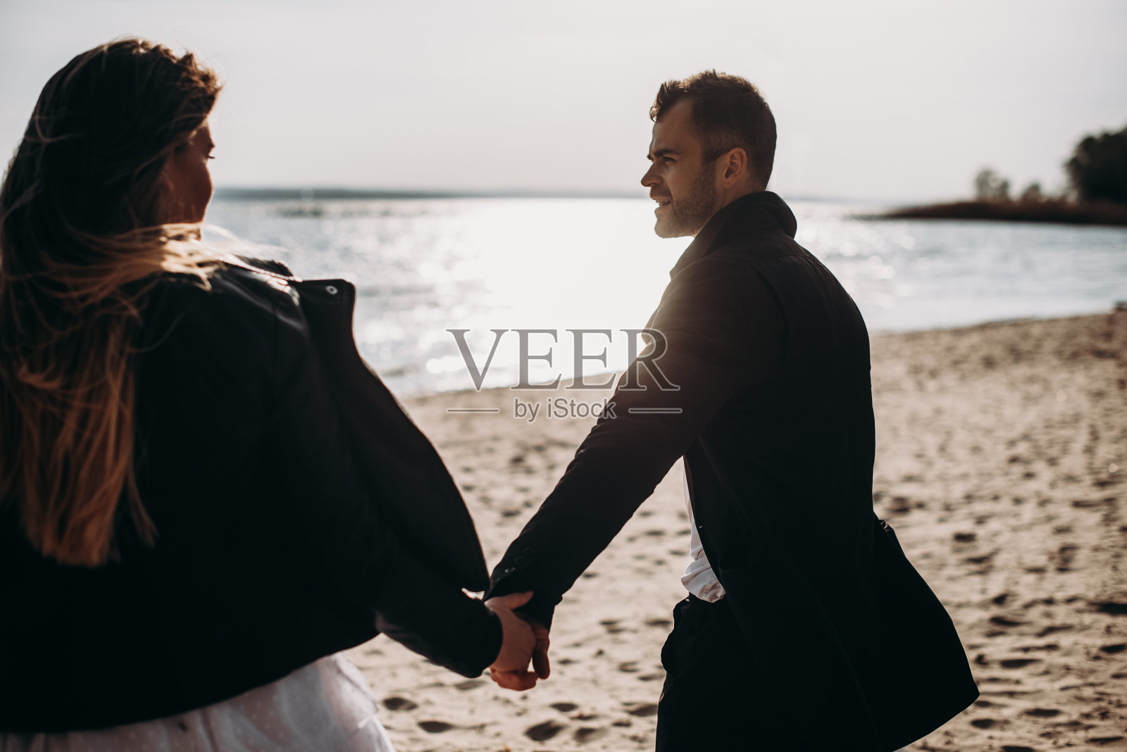 顽皮的年轻潮夫妇在日落时在海滩上牵着手。照片摄影图片