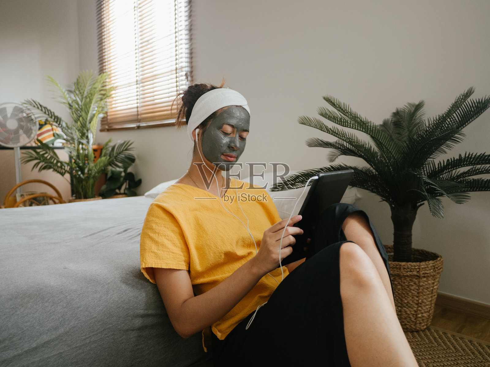 年轻女子敷面膜，在家使用平板电脑。照片摄影图片