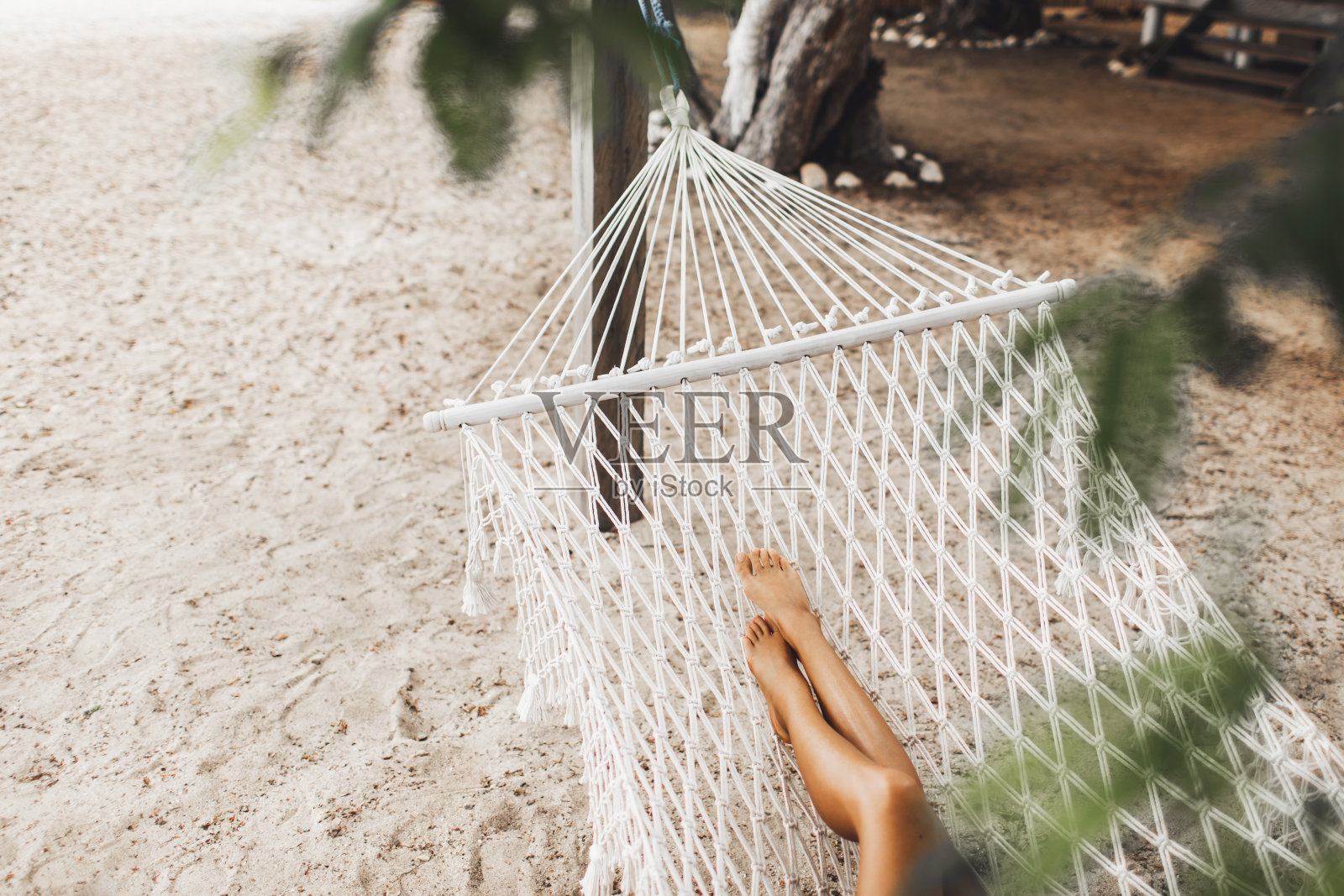 女人赤裸的腿在白色吊床上的热带海滩。旅游、休闲和度假的概念。从以上观点。照片摄影图片