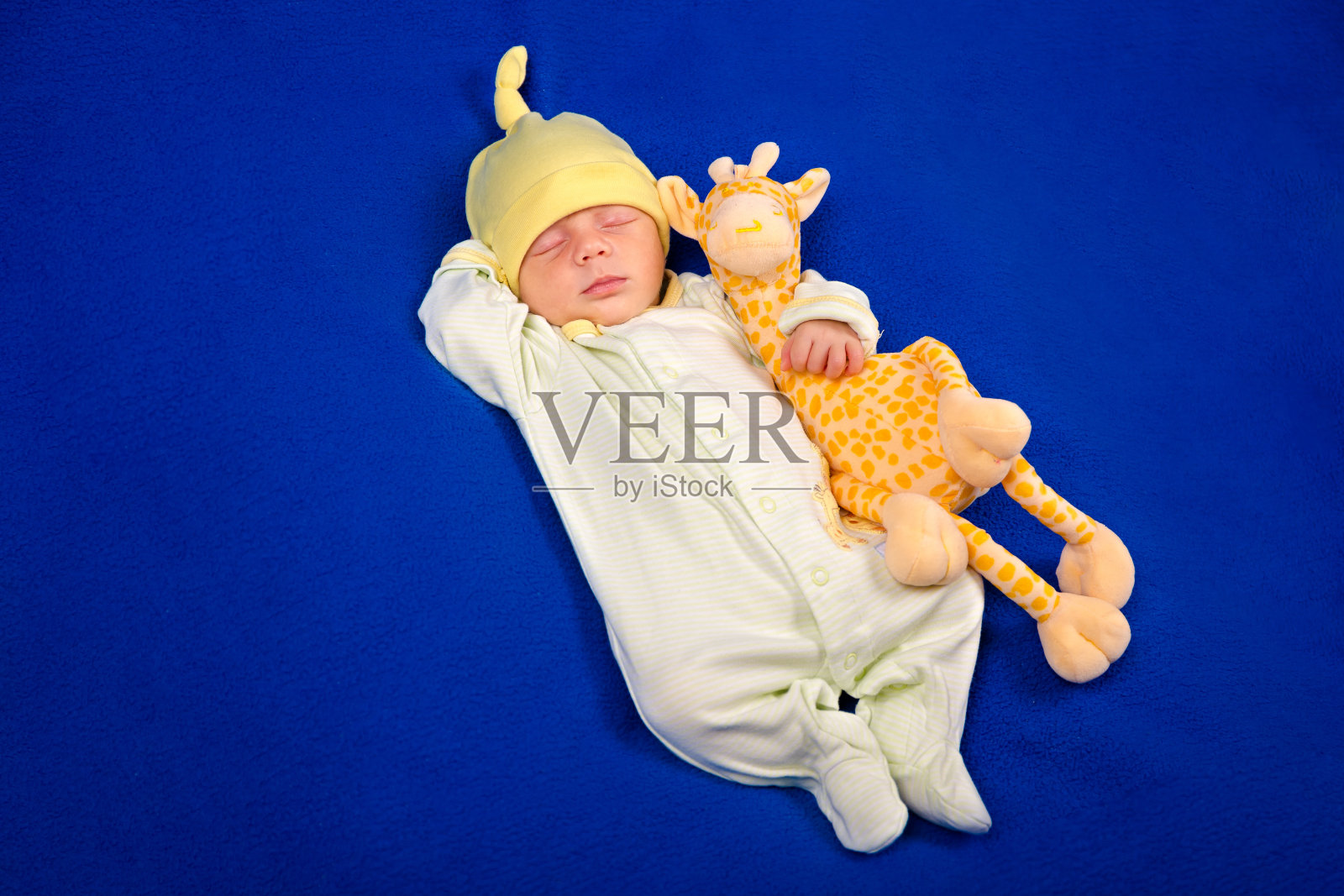 躺在蓝色毯子上，抱着玩具长颈鹿的可爱新生儿，男孩或女孩照片摄影图片