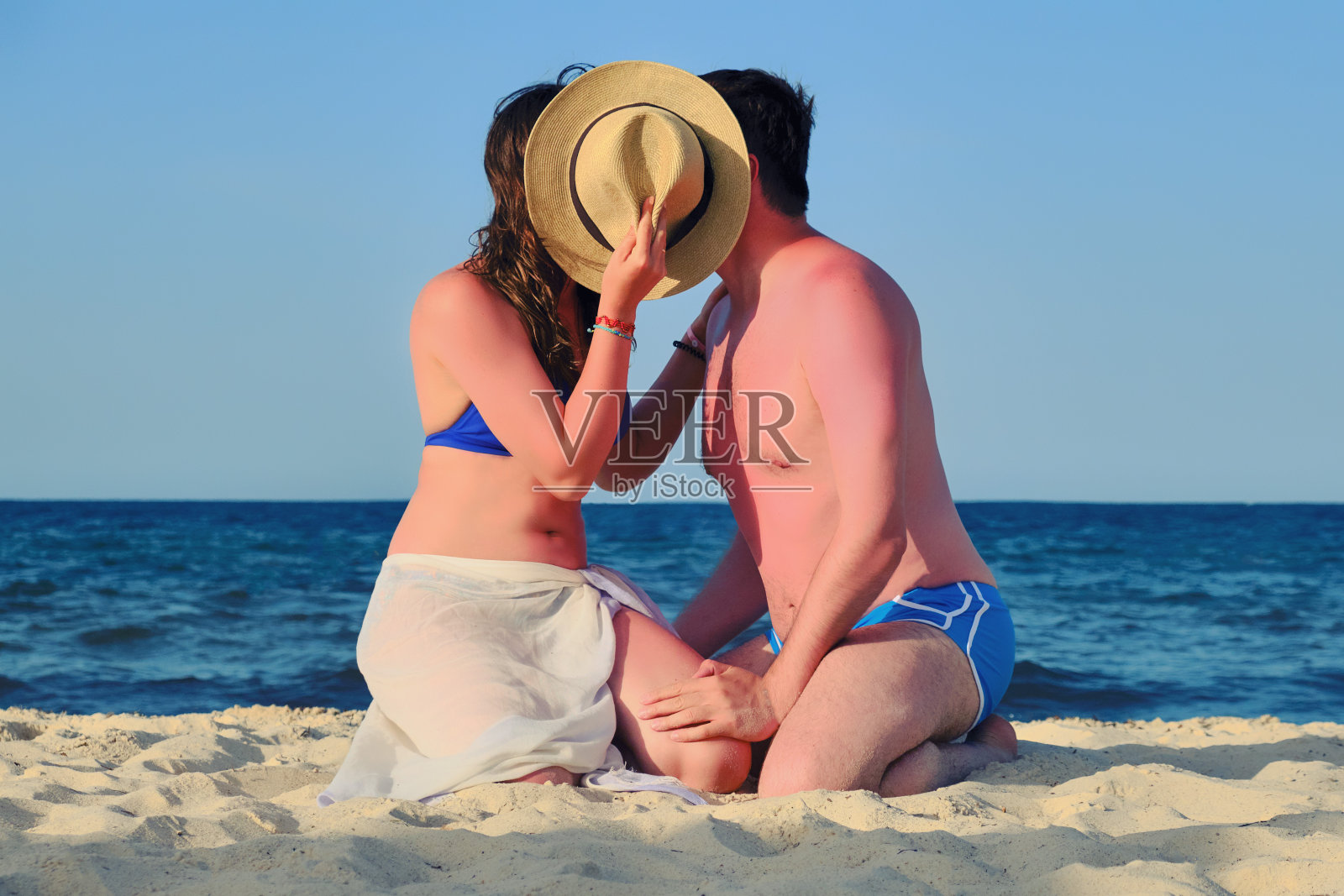 一男一女在海上用帽子盖住自己。海滩上的假日浪漫照片摄影图片