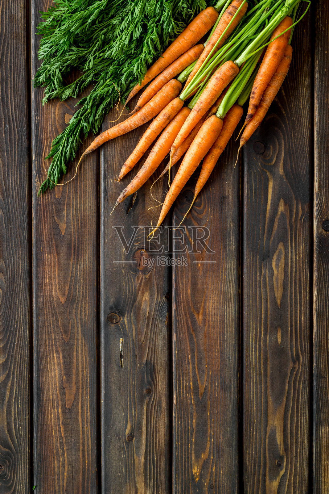 有机胡萝卜，绿色的顶部和叶子在木制的深色桌子上。俯视图照片摄影图片