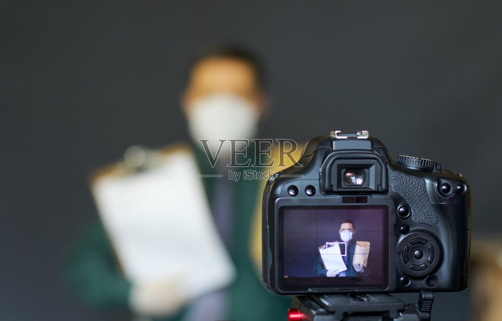一位戴着防护面具的博主用相机给自己拍照。广告产品。焦点放在三脚架上的相机和上面的图像上。其他一切都是模糊的。照片摄影图片