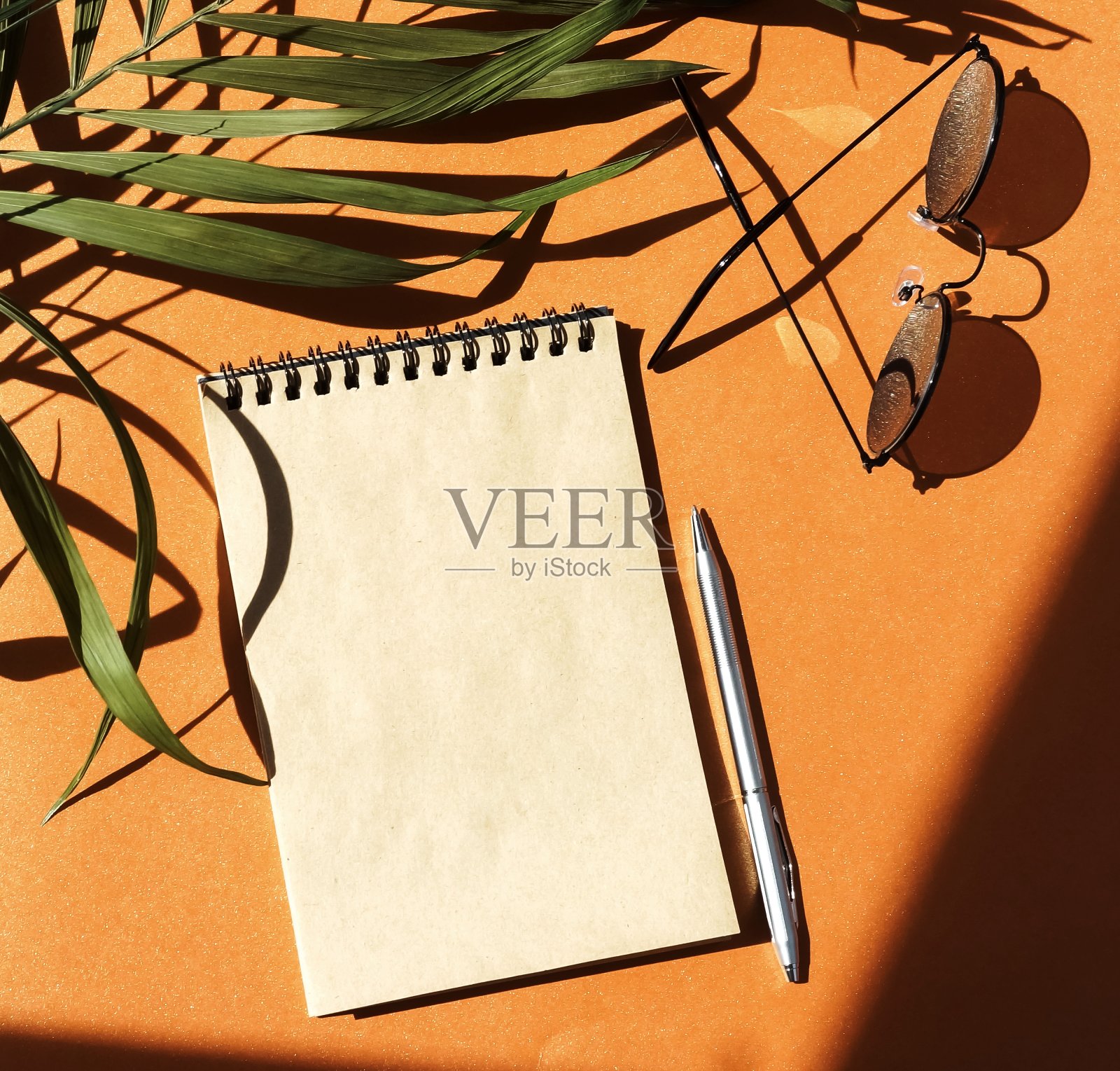 打开笔记本模拟，笔，太阳镜和花的阴影在橙色的背景。本空间照片摄影图片