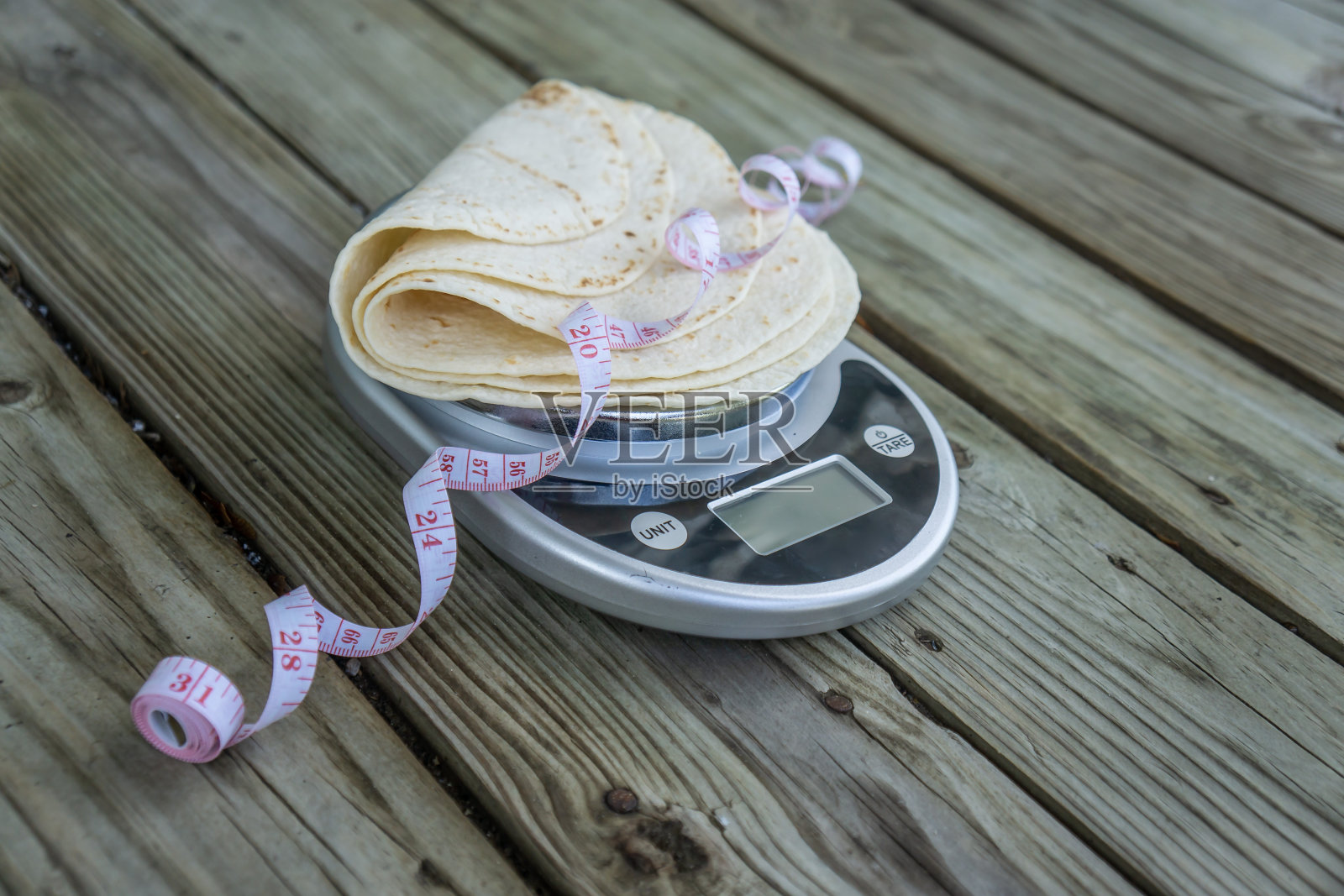食物秤上的低碳水化合物玉米饼，用卷尺在木头背景上测量。空白空白空间的文本或复制空间。生酮和低碳水化合物饮食的健康食品趋势。纯玉米饼，高纤维。照片摄影图片