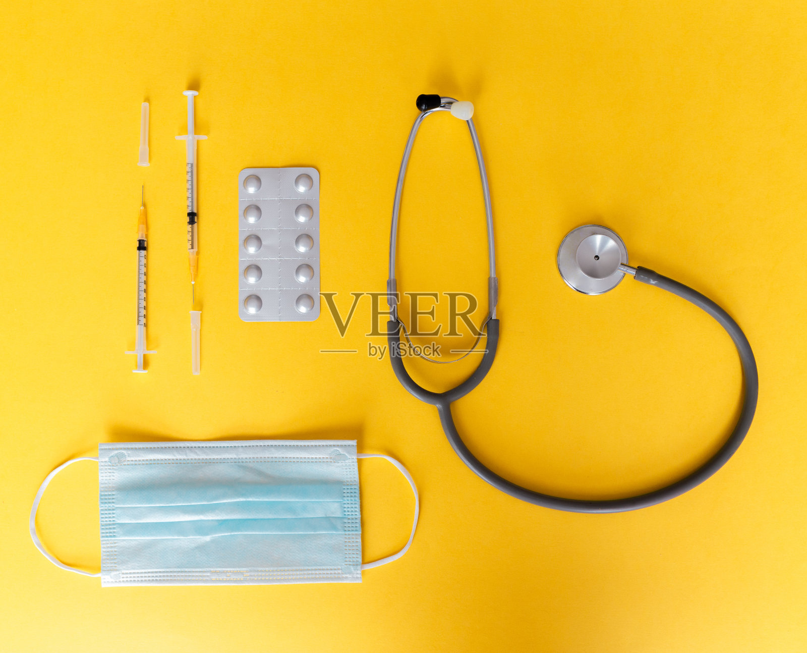 俯视图的医疗概念，黄色背景的听诊器、注射器、口罩和药片，用于预防冠状病毒。Covid-19工具包。本空间照片摄影图片