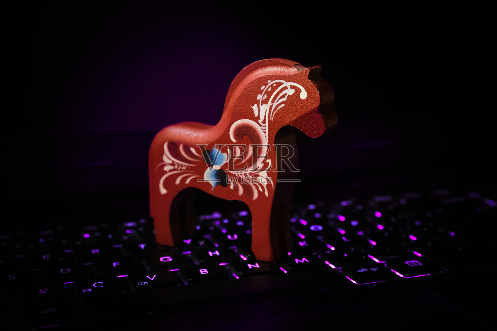 紫色背光笔记本键盘上的木马。电脑黑客，安全，网络犯罪和恶意软件的概念。照片摄影图片