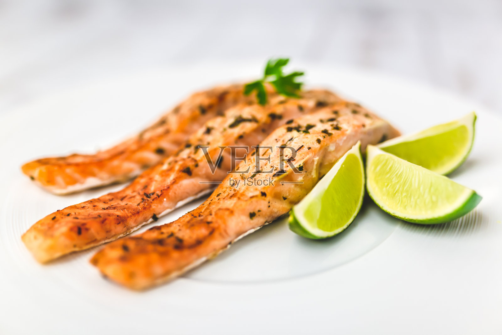 烤充满活力的三文鱼片在一个盘子与香草，奶油酱制成的黄油，大蒜，和蔬菜。白色木桌上放着三文鱼和楔形酸橙。照片摄影图片