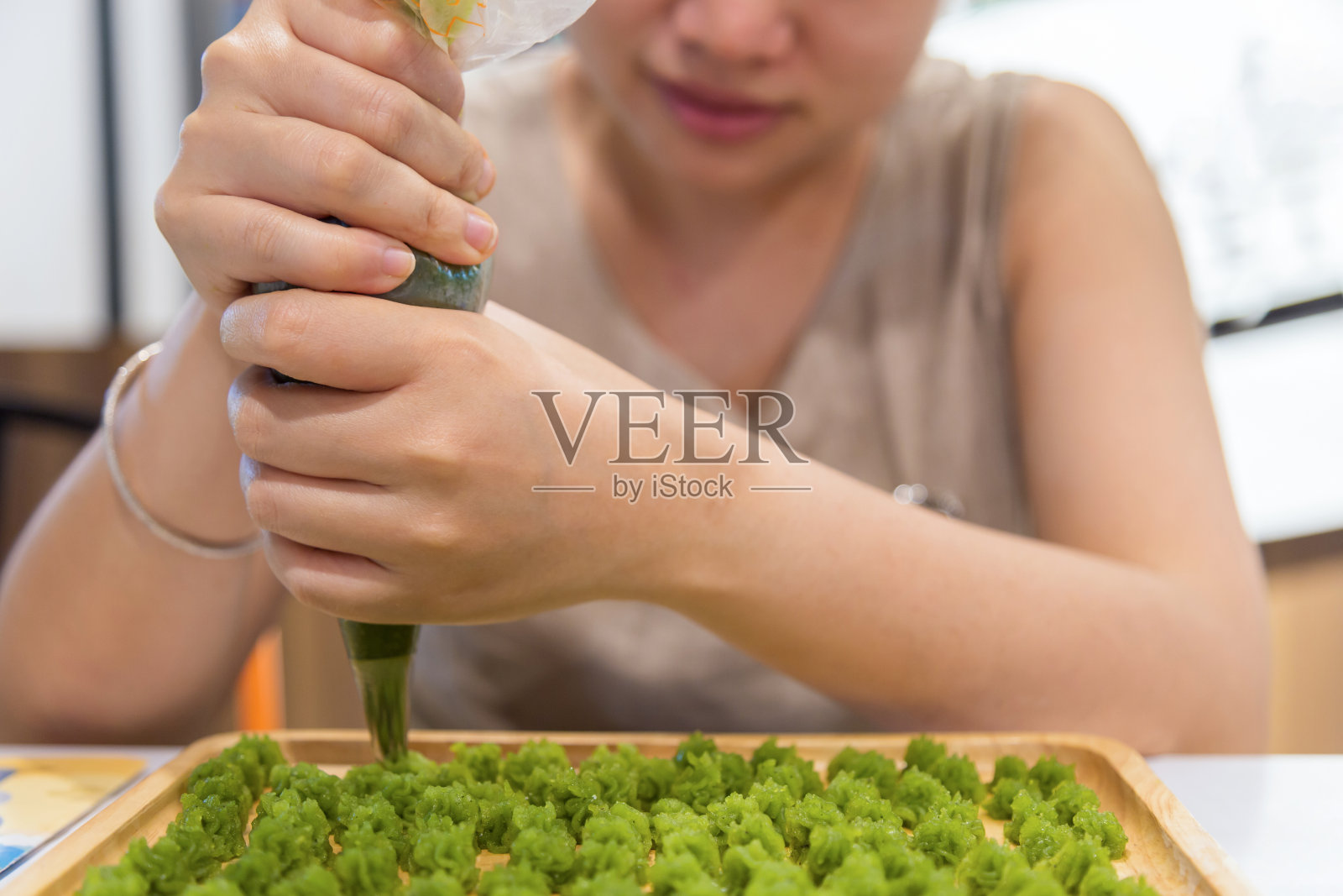 近看美丽的亚洲妇女在休闲服装使用糕点袋填充热熔在木制托盘制作A-lua或Allure泰国手工糖果。照片摄影图片