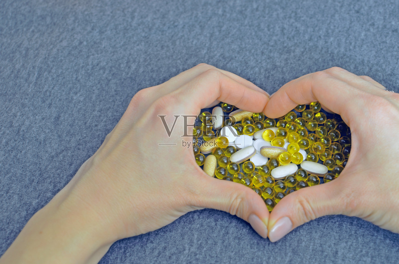 女人的手做成了一个心形。白色和黄色药片。作为广告的特别优惠模拟。医疗保健理念。副本的空间。灰色背景上的文字或标识的空白位置。照片摄影图片