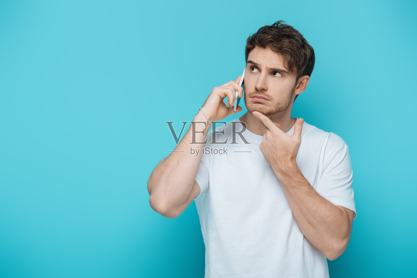 一个深思熟虑的家伙一边用智能手机说话，一边在蓝色背景下看向别处照片摄影图片