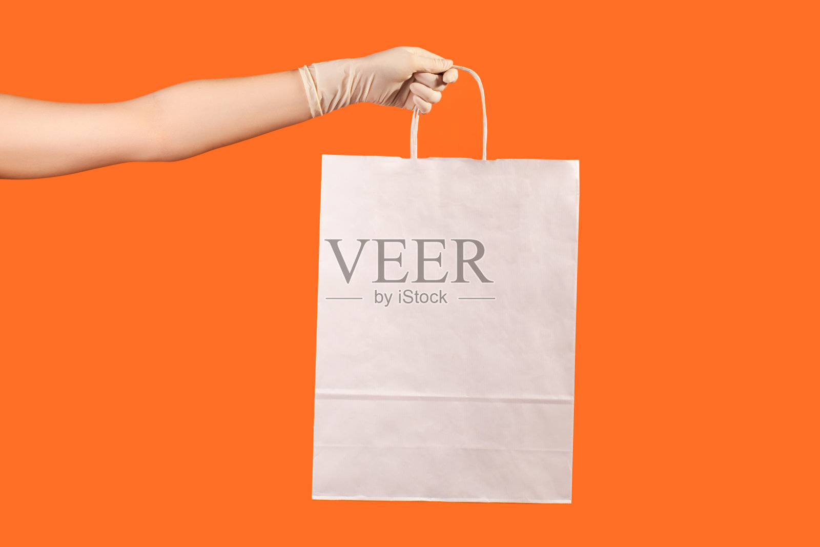 侧面特写的人的手在白色的外科手套拿着和显示白色的购物袋。照片摄影图片