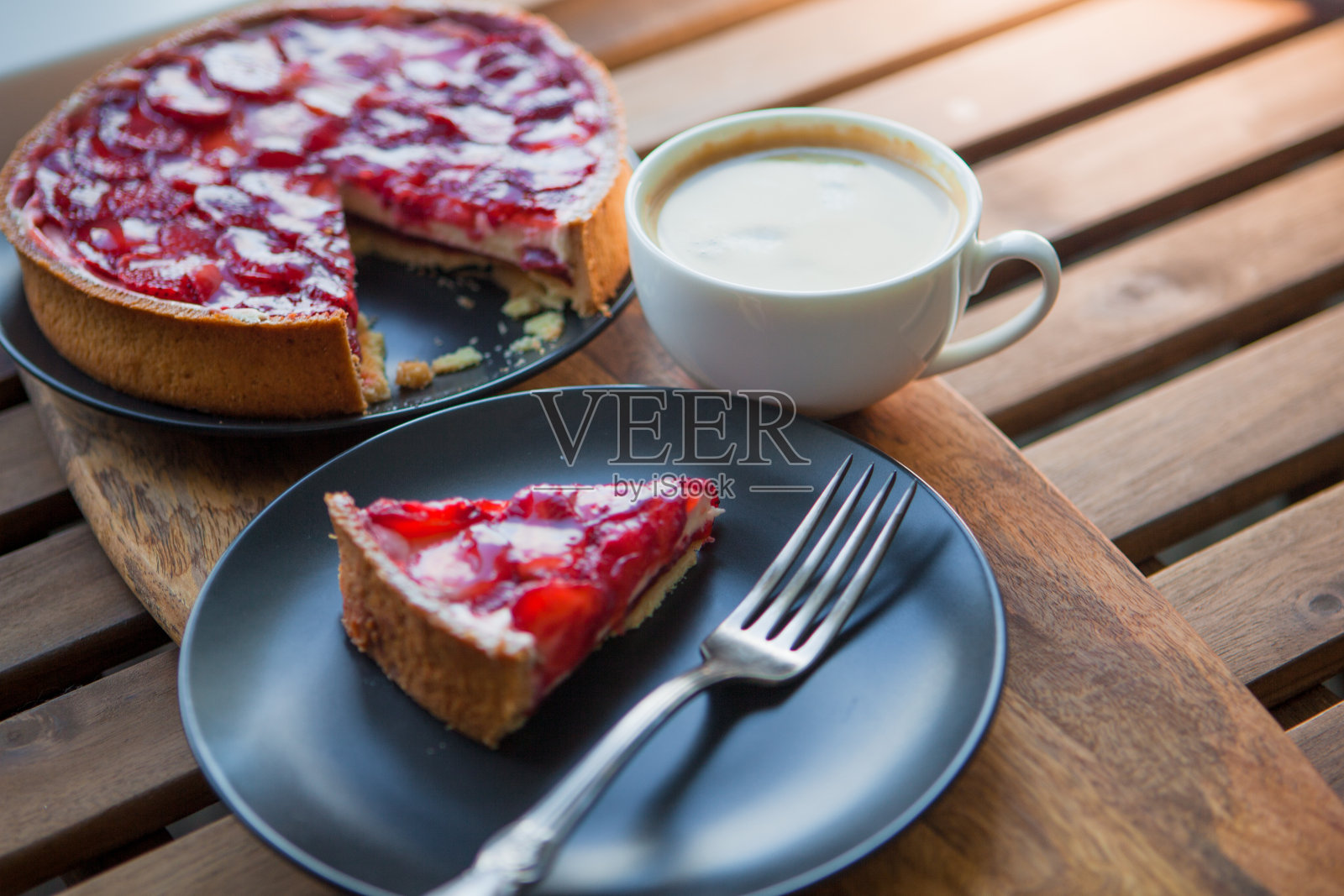 静物与一杯咖啡和草莓甜点，芝士蛋糕与果冻上的浆果片。照片摄影图片