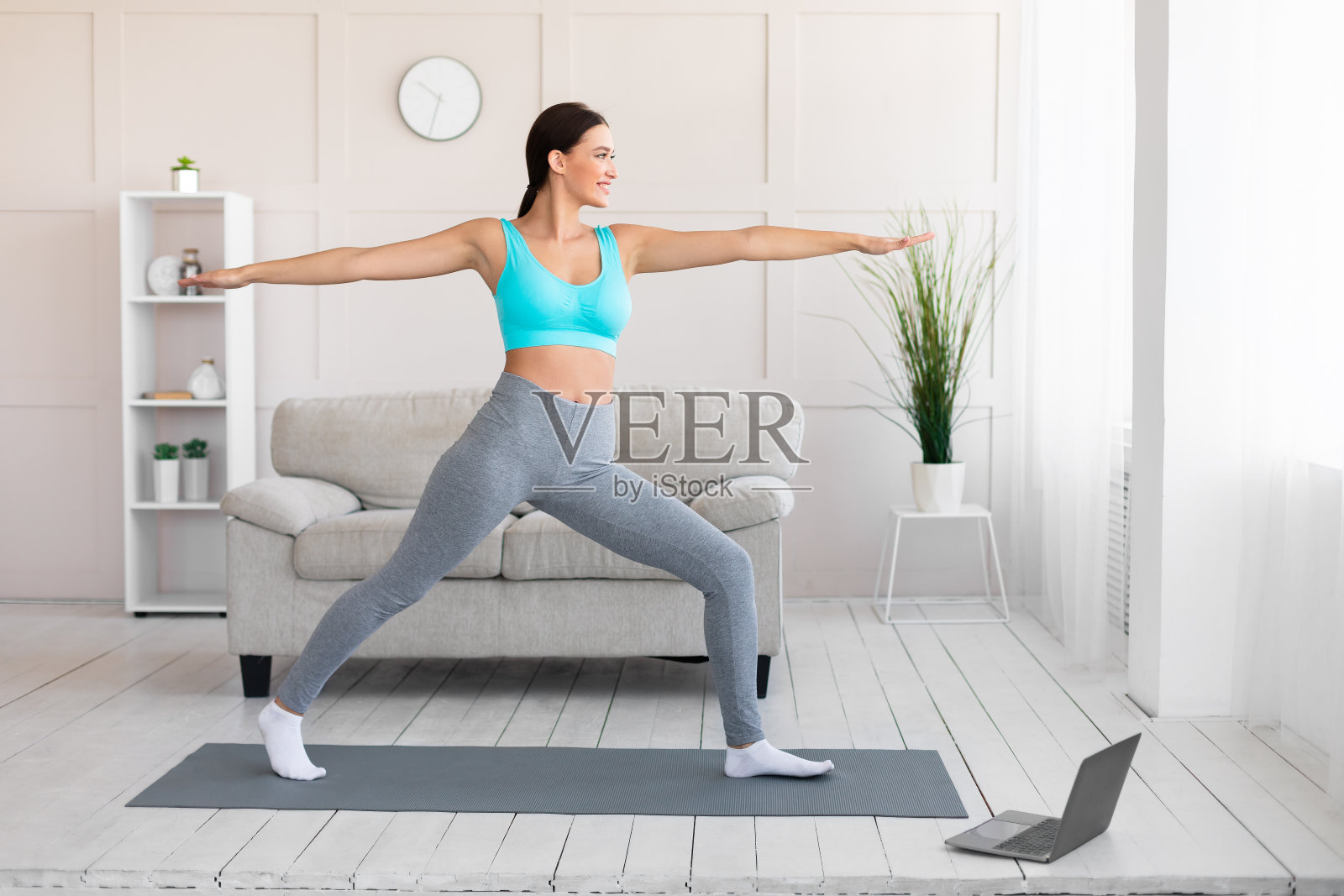 一个女人在用笔记本电脑做瑜伽，站在室内的战士姿势照片摄影图片