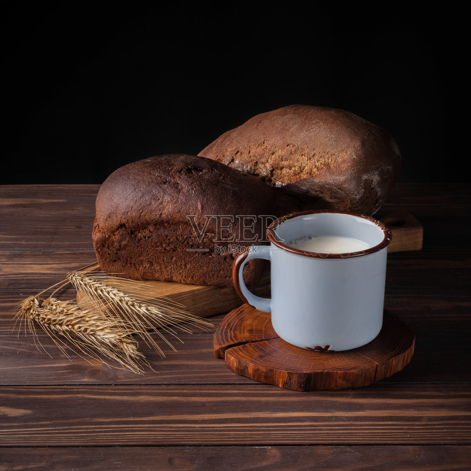 木桌上放着面包、小穗和一杯牛奶，这是一种质朴的静物画照片摄影图片