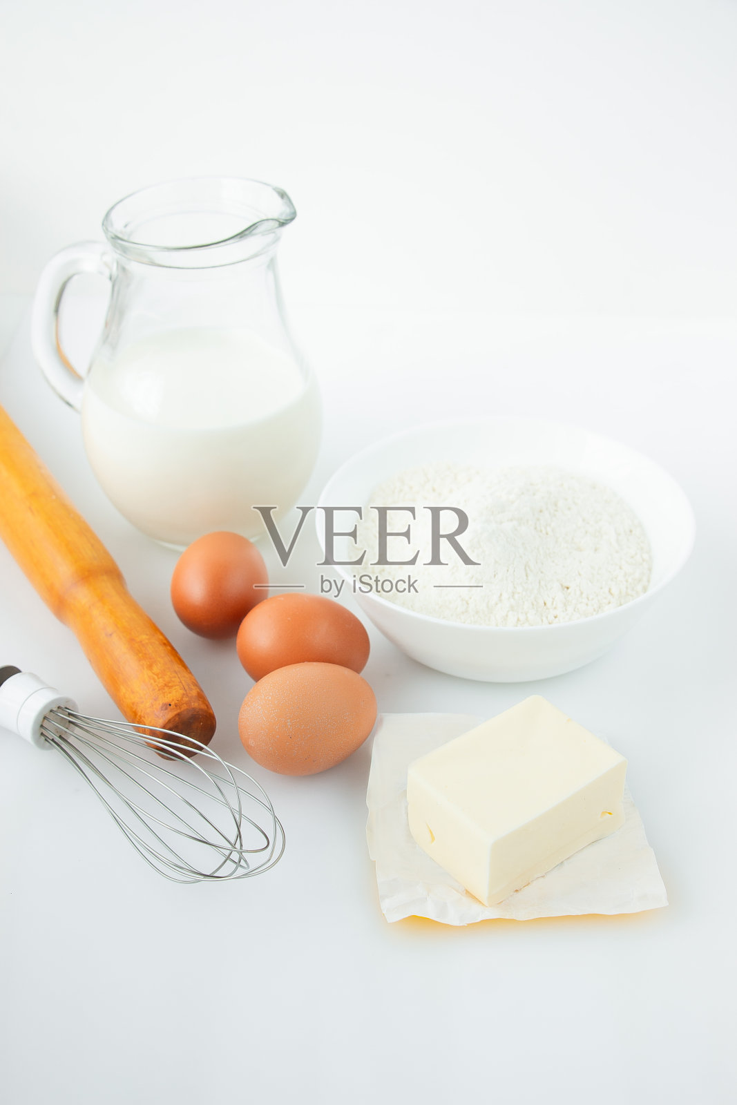 将牛奶、鸡蛋、面粉、擀面杖、黄油和打蛋器放在白色的桌子上。烹饪的食谱。照片摄影图片