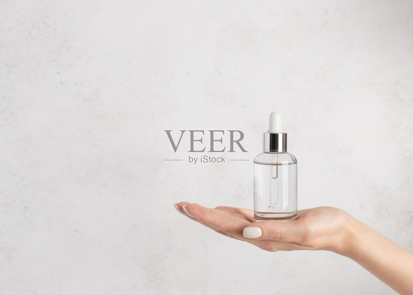 女人的手拿着一个装有保湿精华液的玻璃瓶。照片摄影图片