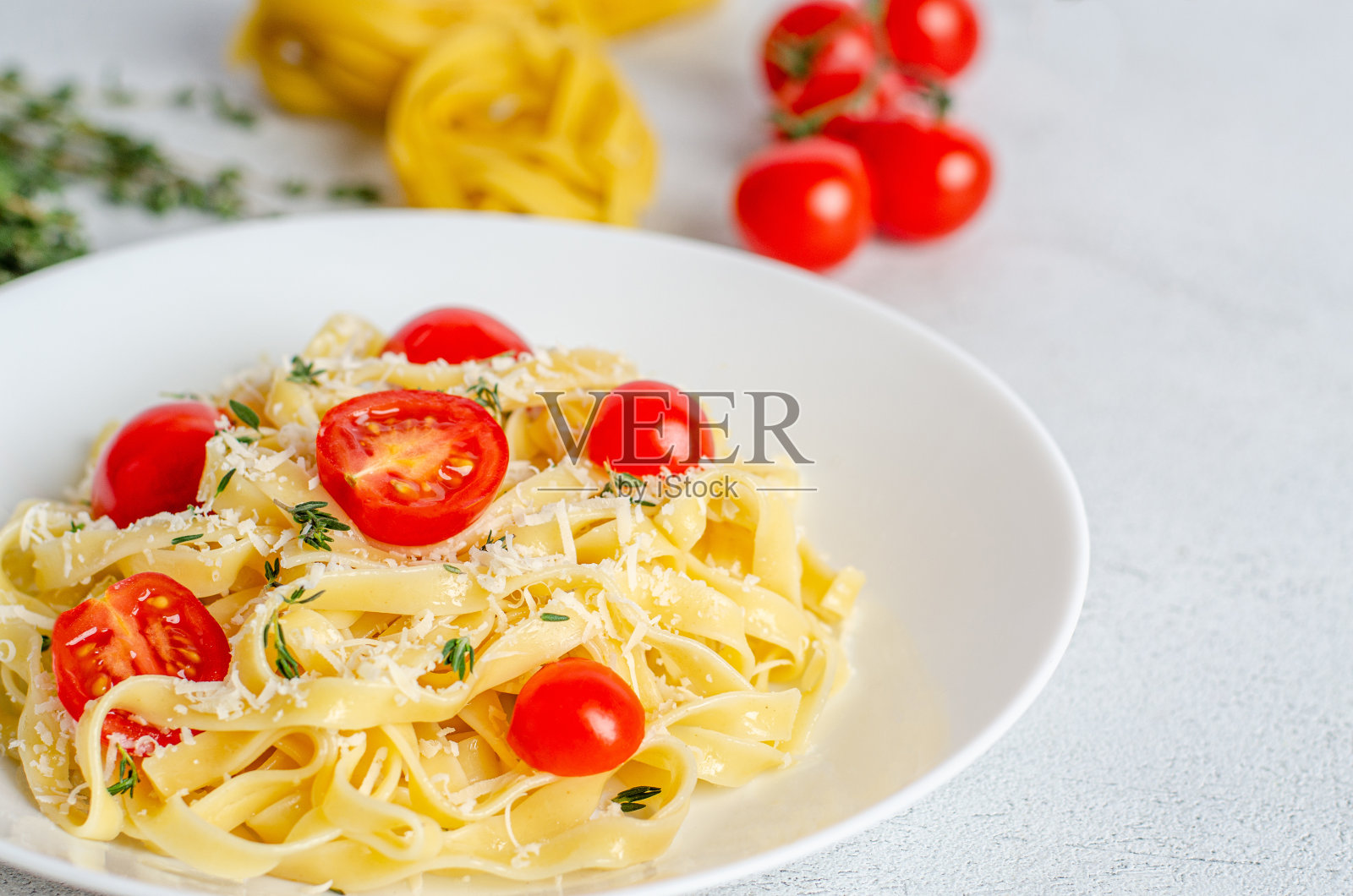 用西红柿，百里香，帕尔马干酪自制意大利面，白色盘子，背景光线。照片摄影图片