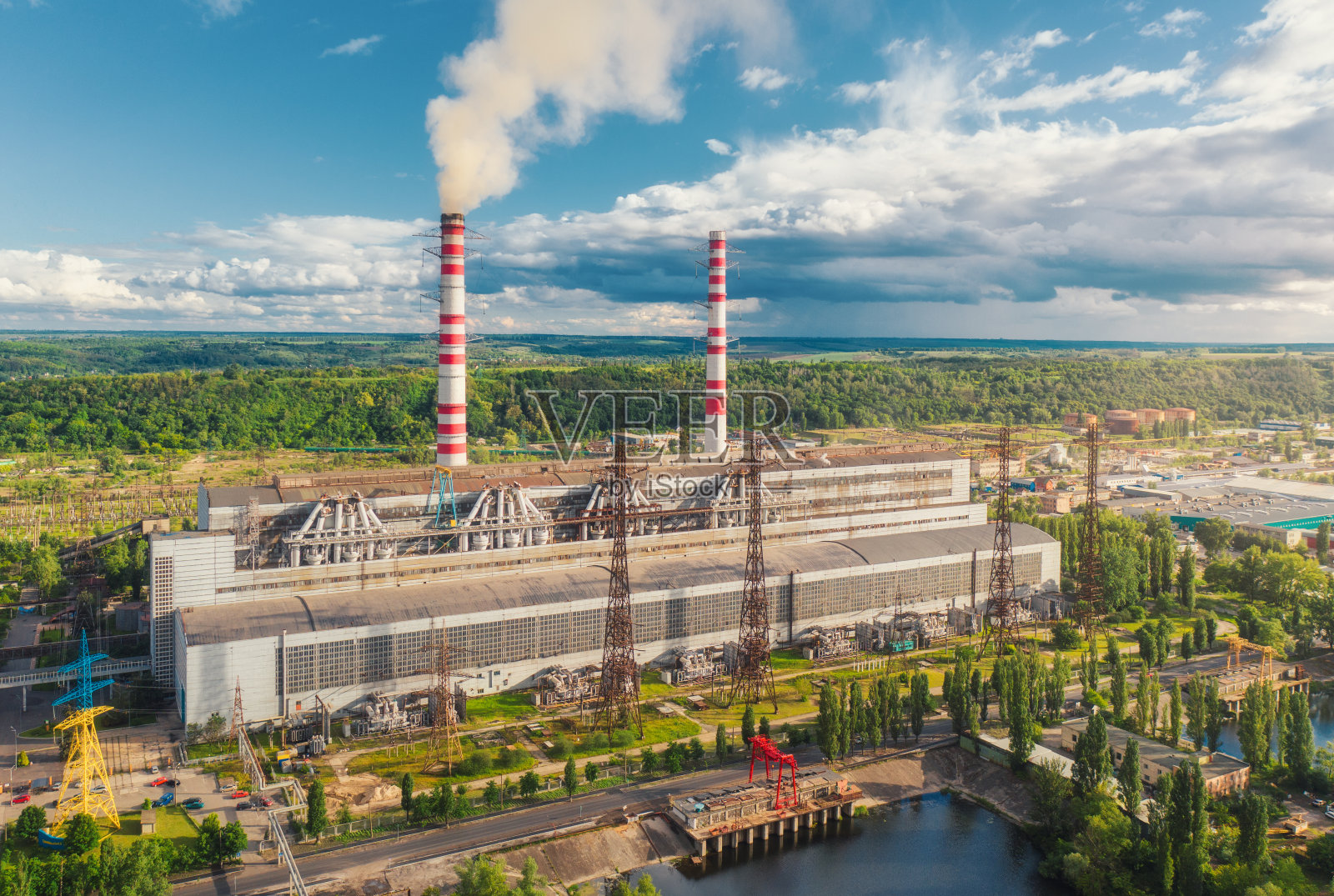 热电站鸟瞰图。工业景观有火电厂，管道有烟，建筑，绿树，夏季日落蓝天有云。前视图。烟囱照片摄影图片