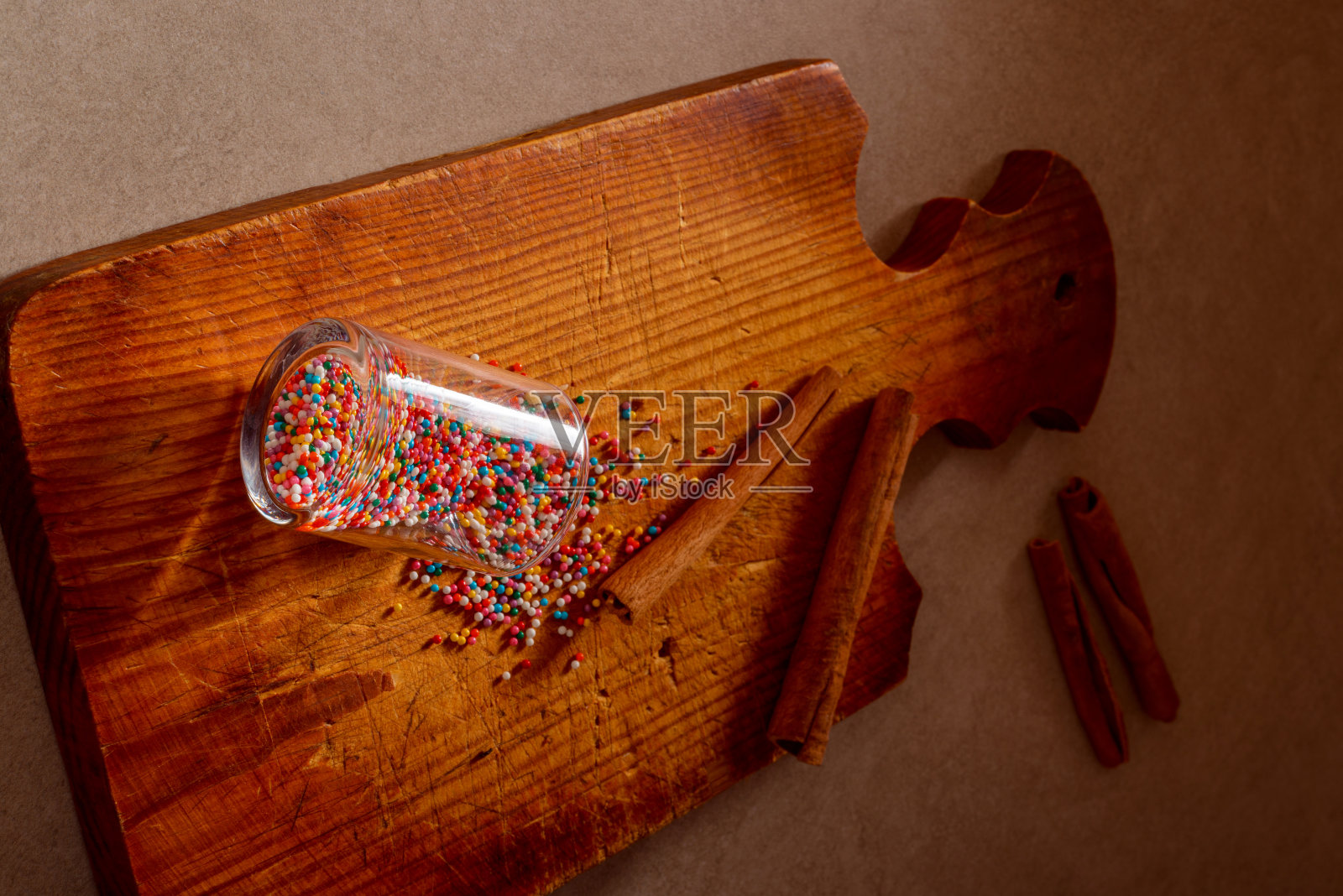 彩色的糖果和糖果从玻璃洒在旧的厨房木板上，肉桂棒。艺术照片选择焦点。圣诞节，烹饪，厨房，食物和家庭烘焙概念照片。照片摄影图片