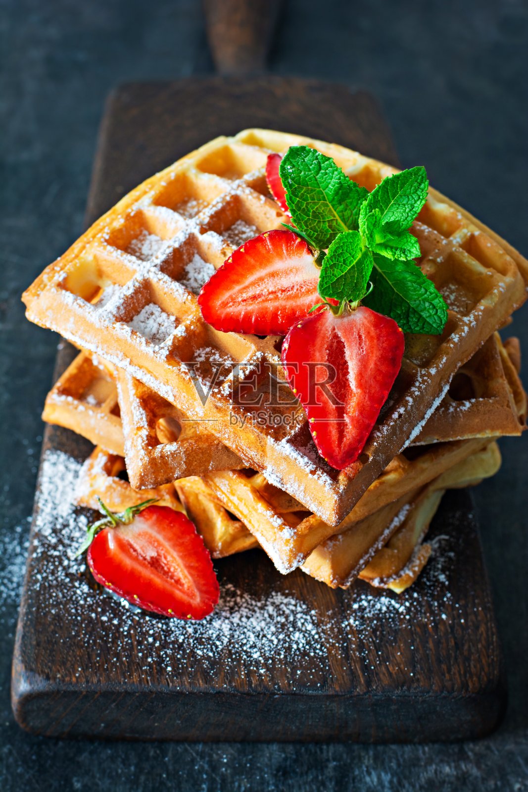 新鲜脆的比利时华夫饼配上成熟的草莓、薄荷和蜂蜜，放在木板上，背景为黑色。照片摄影图片