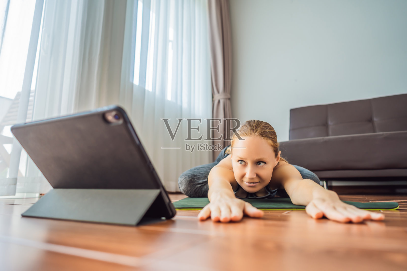 健身女性在家里的地板上锻炼，在平板电脑上看健身视频。人们上网运动是因为冠状病毒照片摄影图片