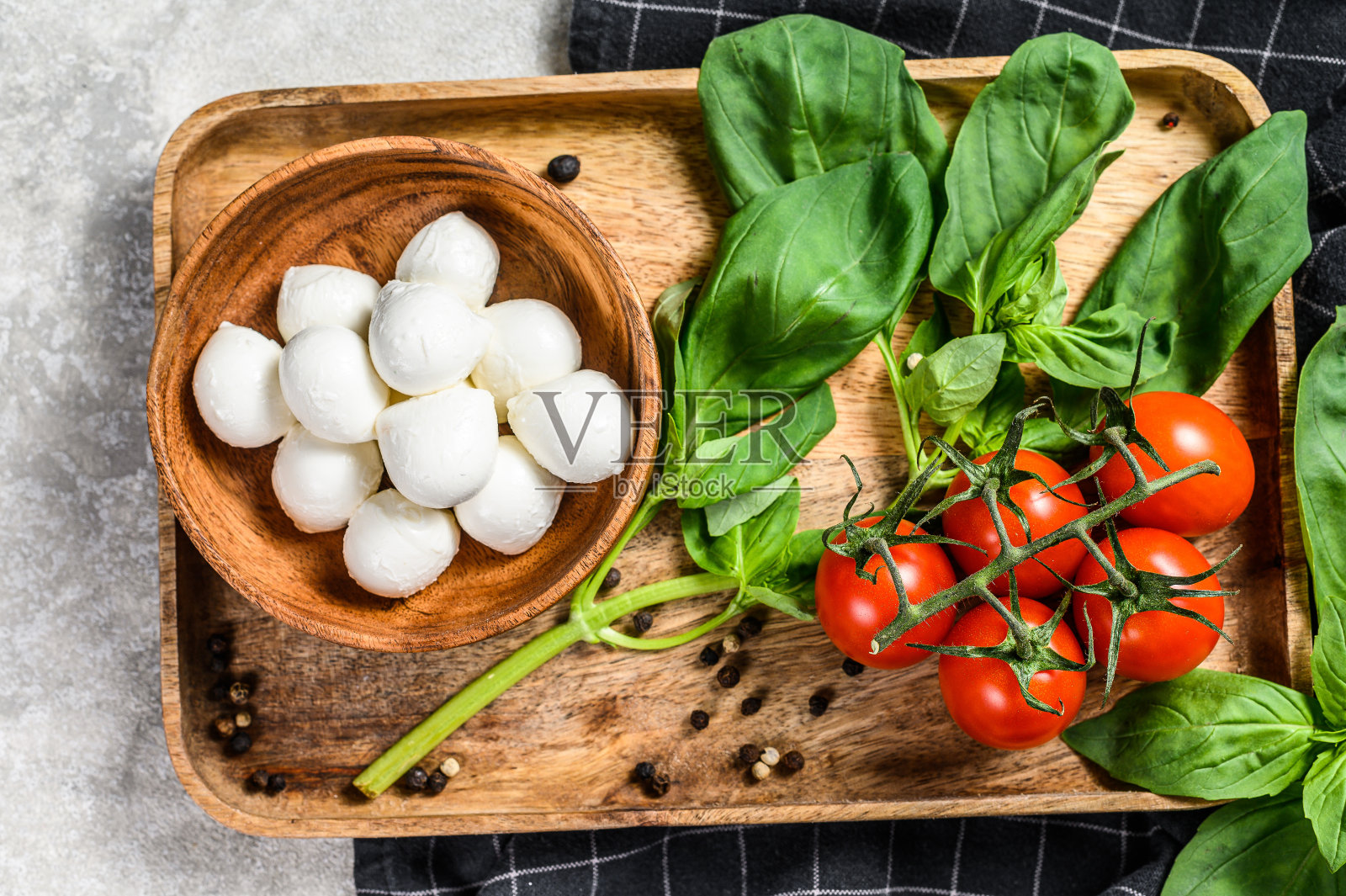 卡普里沙拉的配料:木碗里的迷你马苏里拉奶酪、罗勒叶和樱桃番茄。灰色的背景。俯视图照片摄影图片