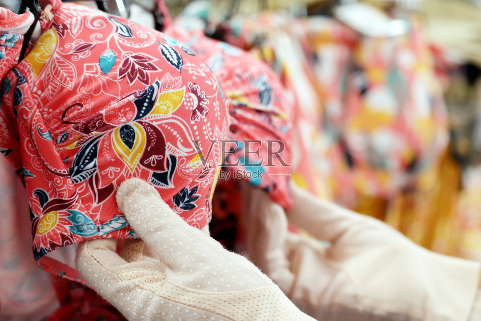 戴防护手套的女人在内衣店选择挂在架子上的泳衣照片摄影图片