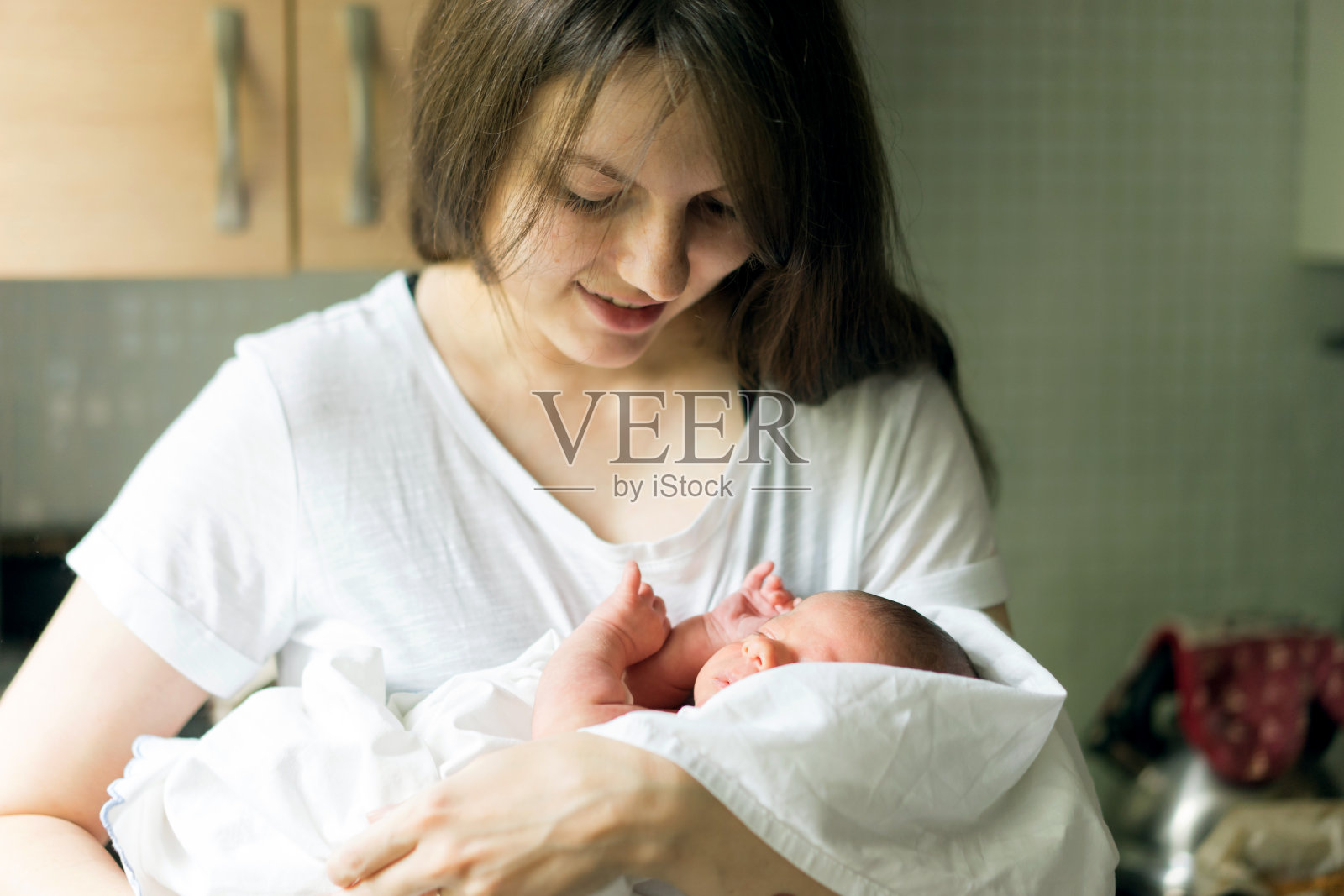 一位母亲怀里抱着刚出生的男婴，正在厨房里给他喂奶照片摄影图片