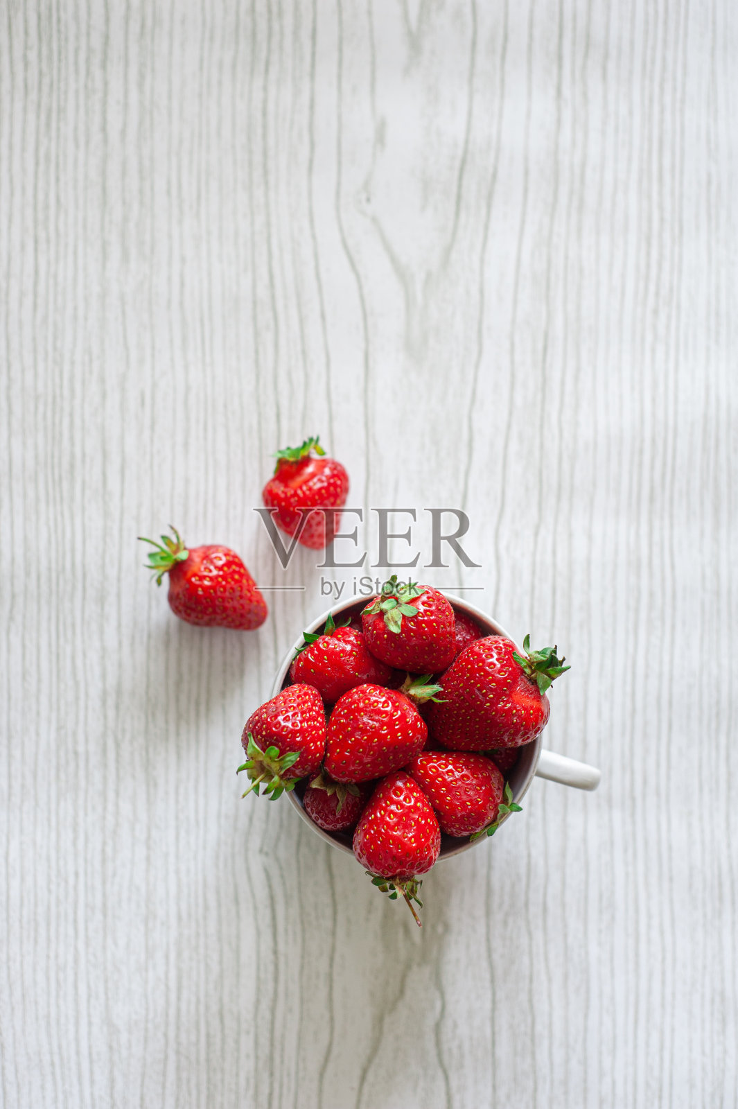 杯子里的草莓放在一个浅色的木制背景上。从以上观点。照片摄影图片