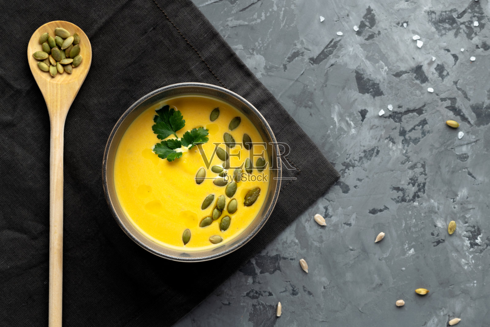 灰色背景的南瓜汤，配勺子和种子。前视图。照片摄影图片