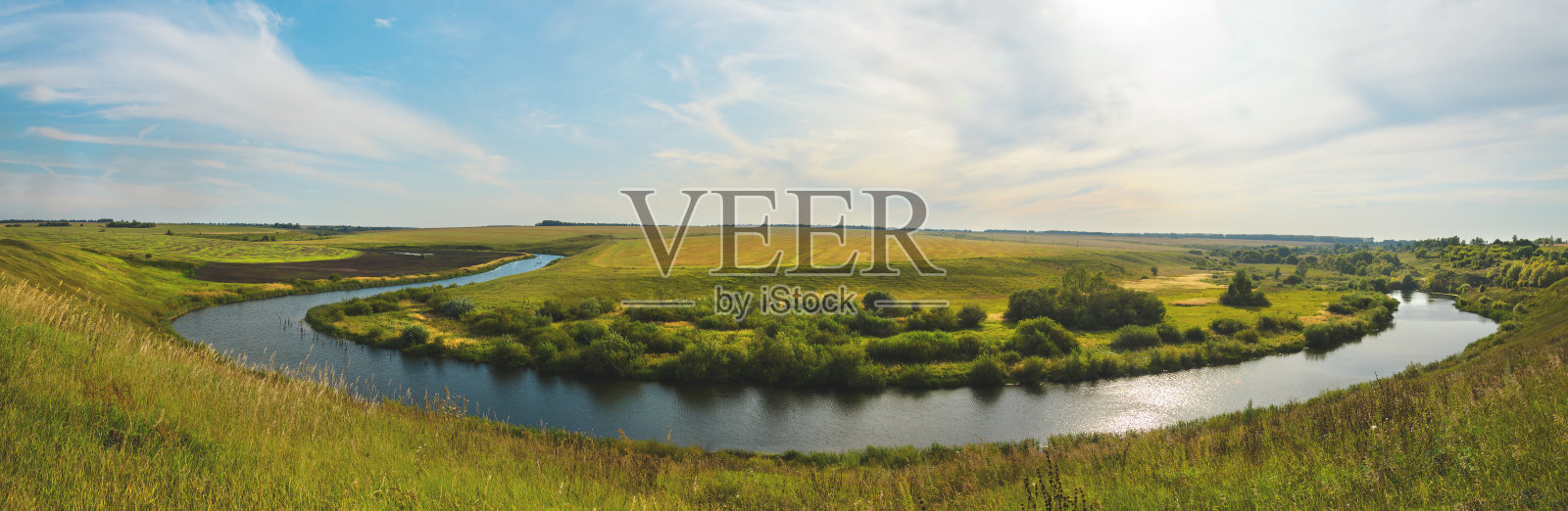 阳光明媚的日落的河流和绿色的草地与树木的背景。照片摄影图片