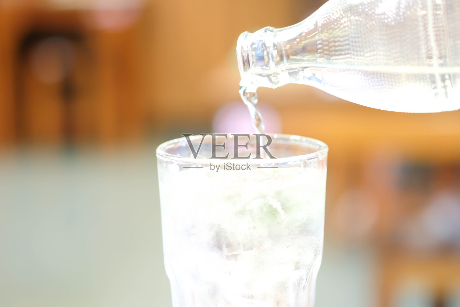 水瓶将水倒入木桌上加冰的玻璃杯中。照片摄影图片