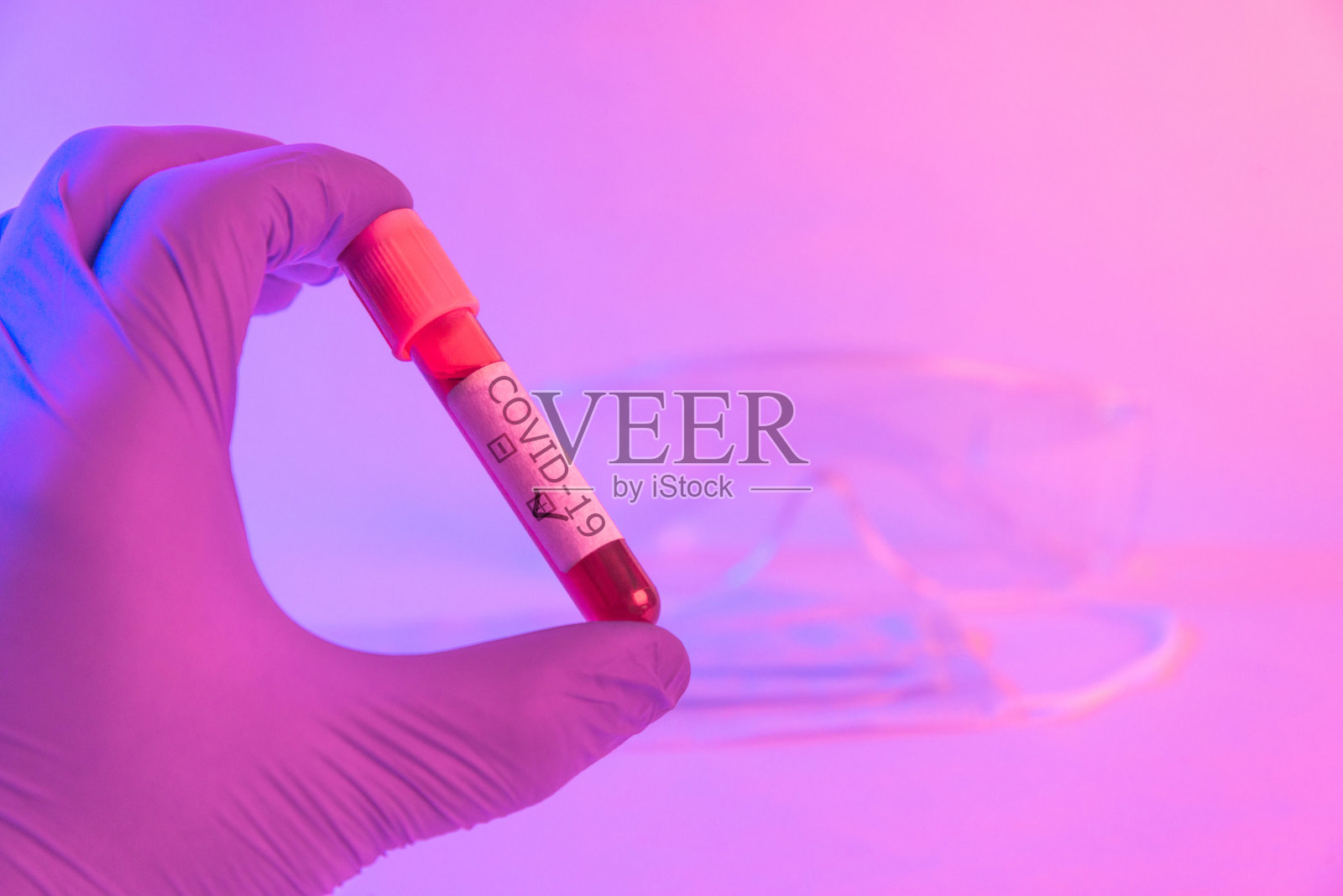 医生手戴手套，在霓虹灯下拿着covid-19阳性血液管。照片摄影图片