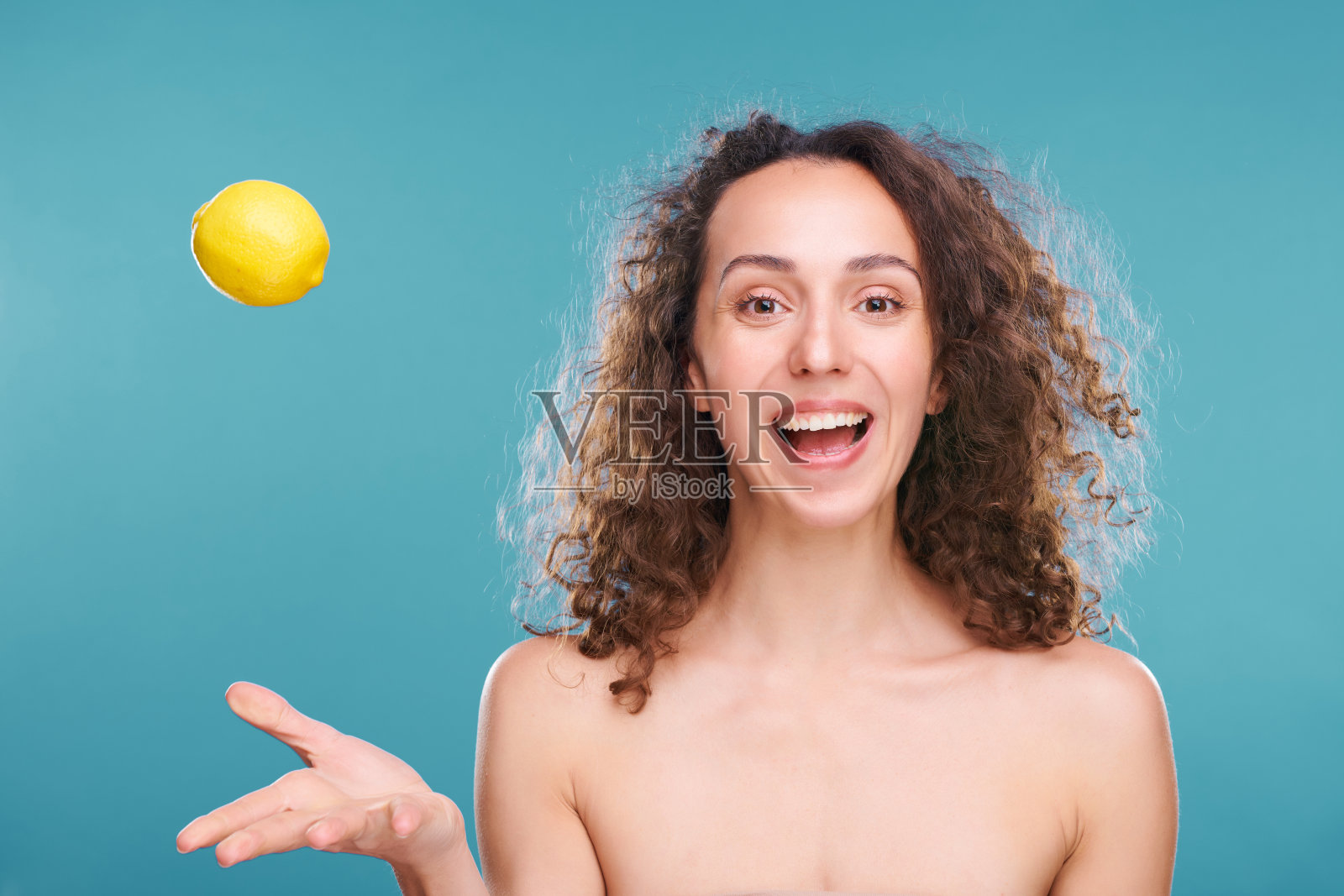 年轻快乐的女人裸露的肩膀和黑色的卷发扔新鲜的柠檬照片摄影图片