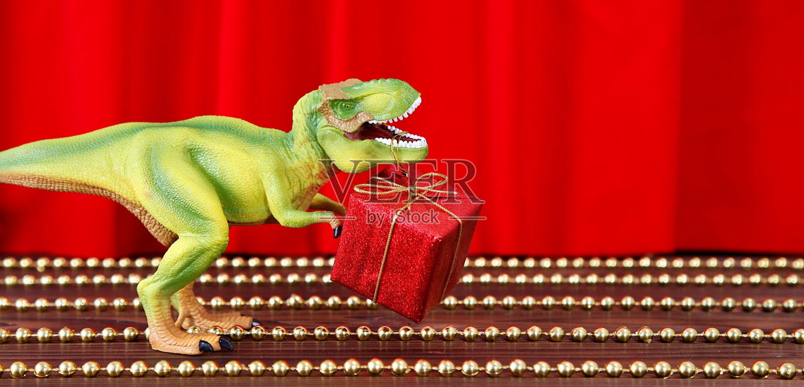 舞台上的塑料恐龙。红色的剧场幕布背景上的红色圣诞礼物龙玩具。有趣的圣诞贺卡。创造性的最小概念。复制空间，文本的自由空间。照片摄影图片