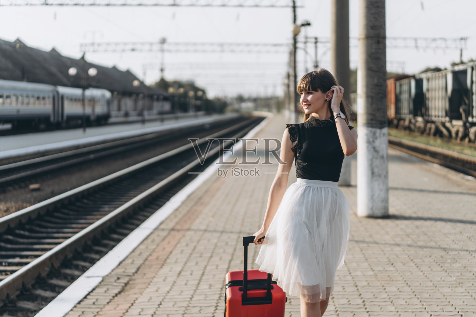 深色头发的女性旅行者带着红色的手提箱走在火车站上照片摄影图片