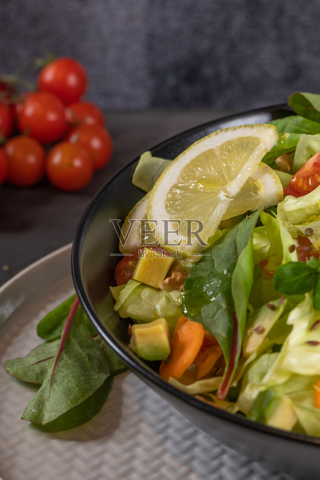 沙拉。春天蔬菜沙拉。新鲜蔬菜沙拉，有西红柿，苹果，坚果，种子和柠檬。橄榄油倒进沙拉碗里照片摄影图片