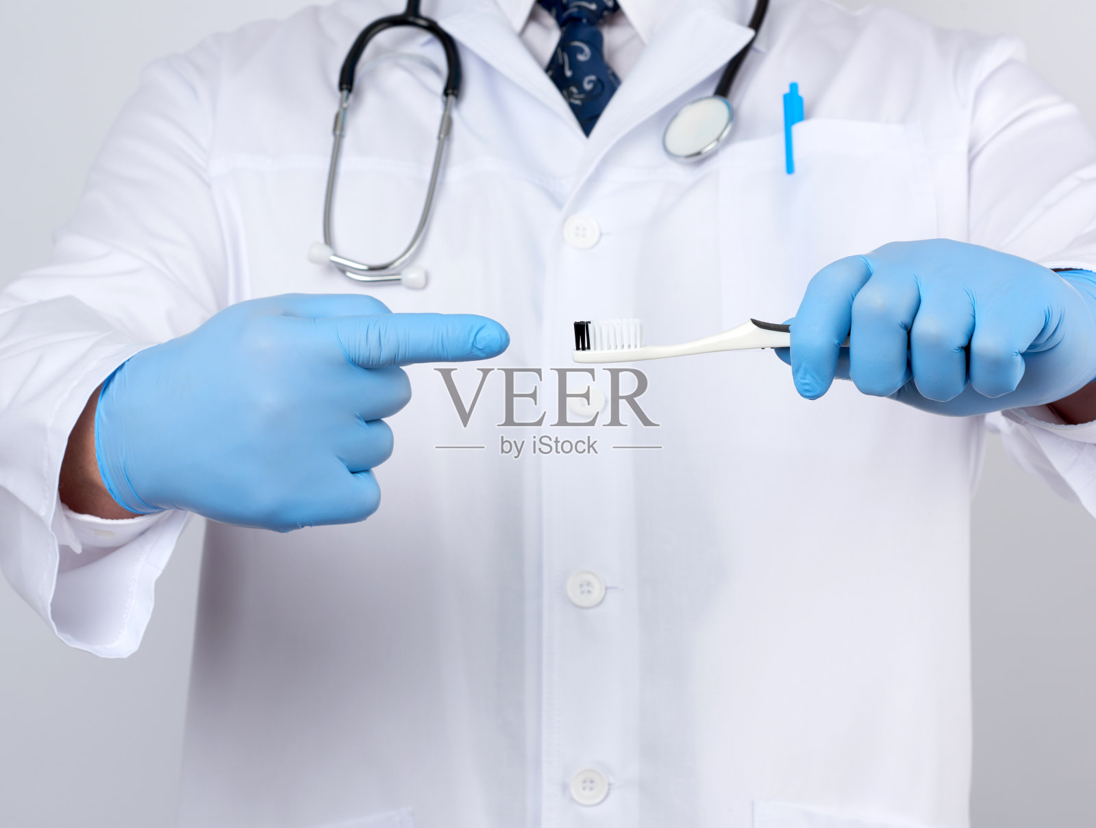 医生治疗师穿着白色长袍制服和蓝色无菌手套站着，手里拿着牙刷照片摄影图片