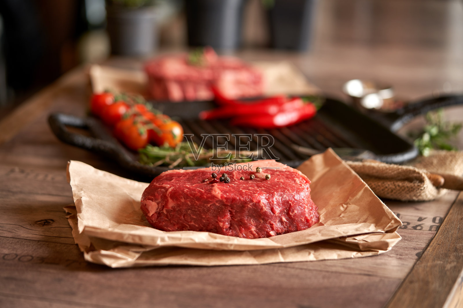 多汁，调味的生肋眼牛排放在食物纸上，旁边放着烤盘，树枝上放着西红柿，大蒜头，红辣椒和香草。浅景深，优质细分牛排。照片摄影图片